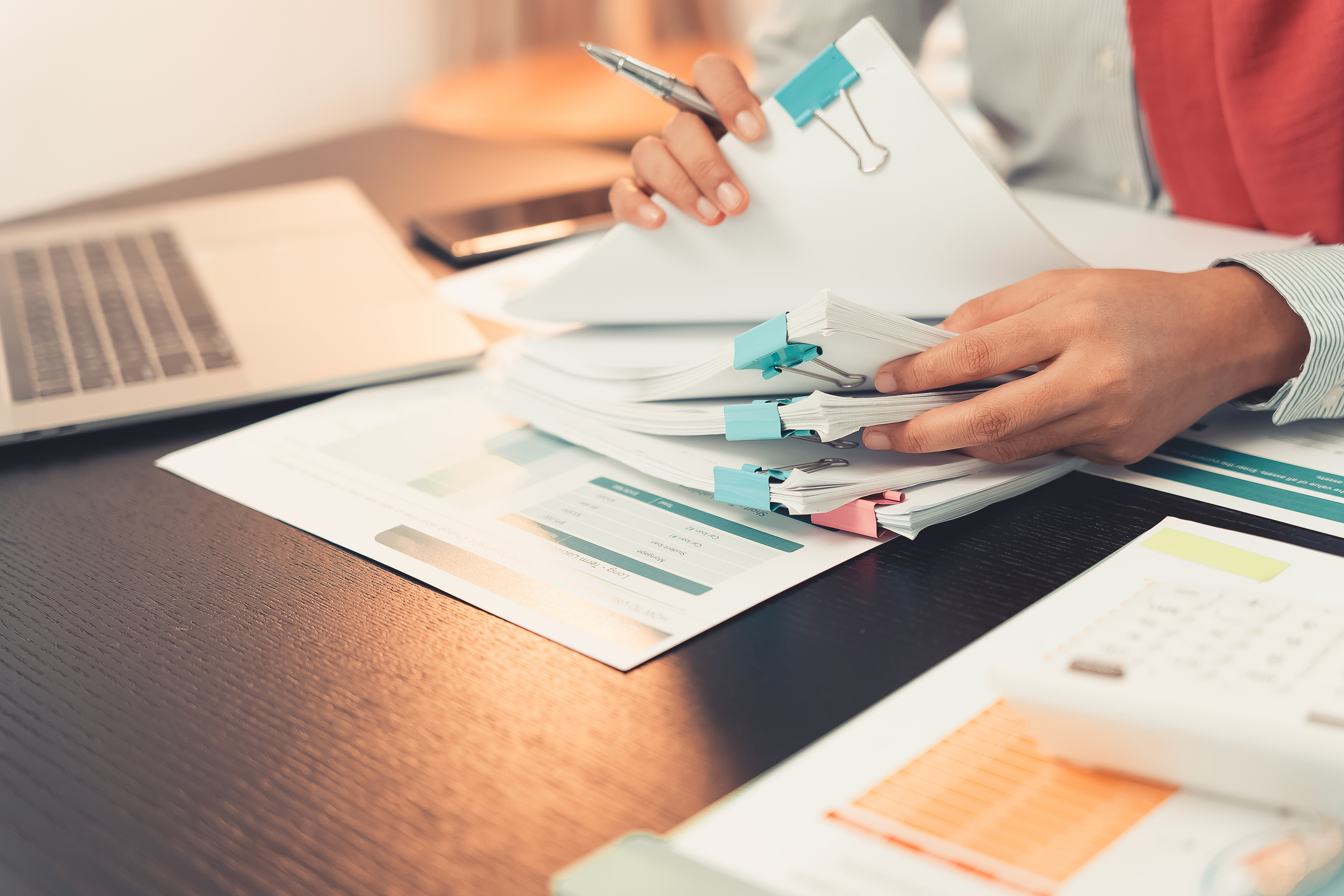 Close-up of someone going through a stack of paperwork at their desk.