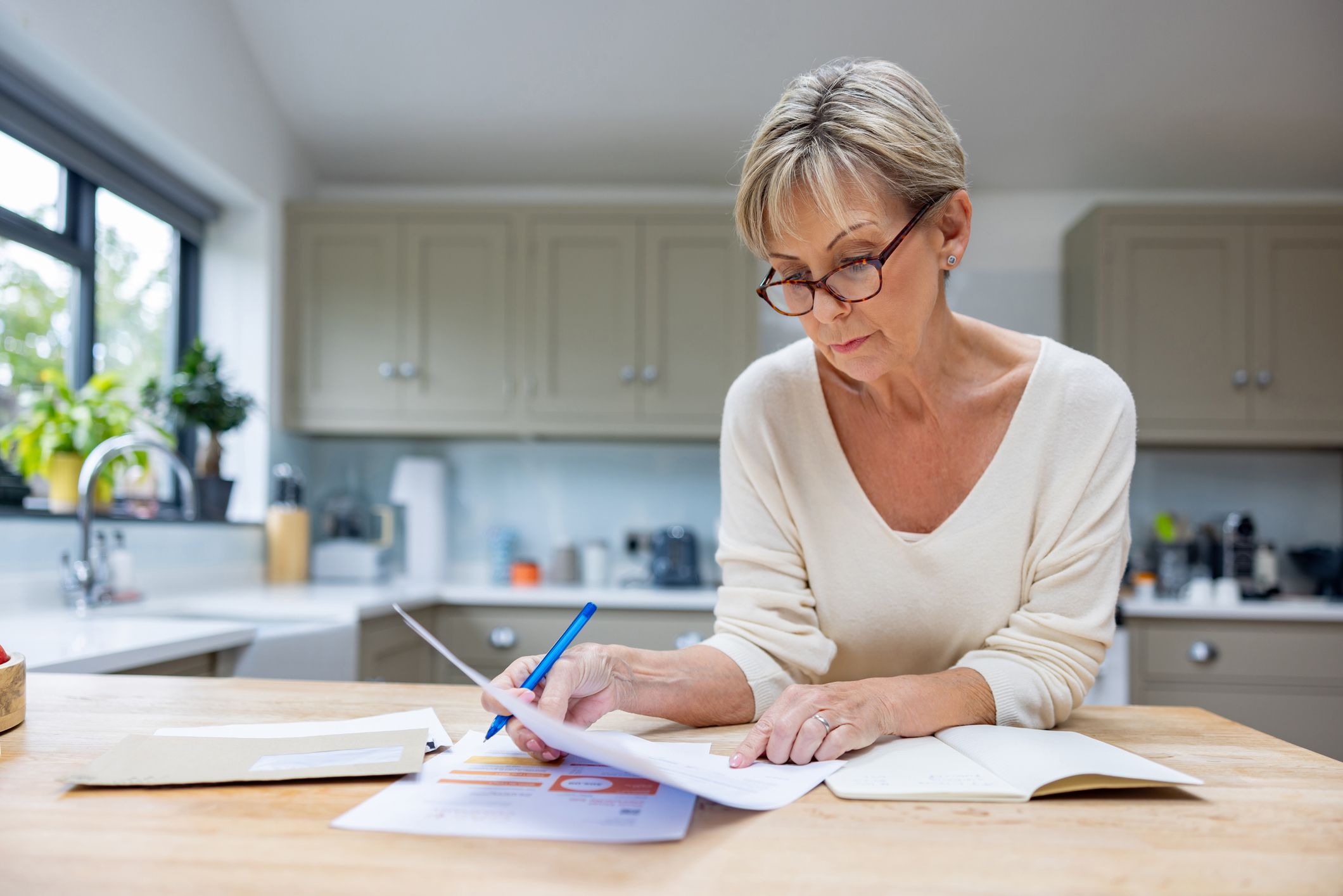 Middle-aged woman reading some paperwork carefully at her kitchen counter.