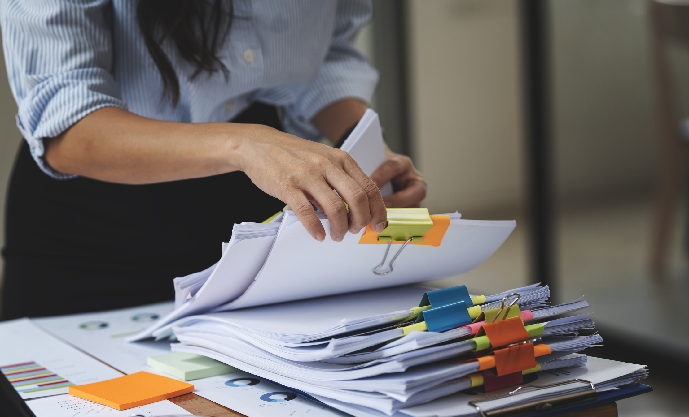 Woman going through stacks of paperwork in an office.