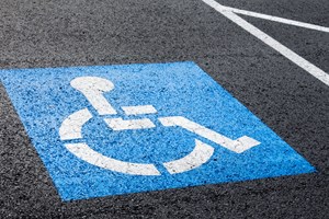 Image of the blue painted symbol on a parking spot indicating that the spot is for handicapped only.  The symbol is a blue square, with the international symbol for handicapped parking in the middle of it.  The black asphalt is clean and new.